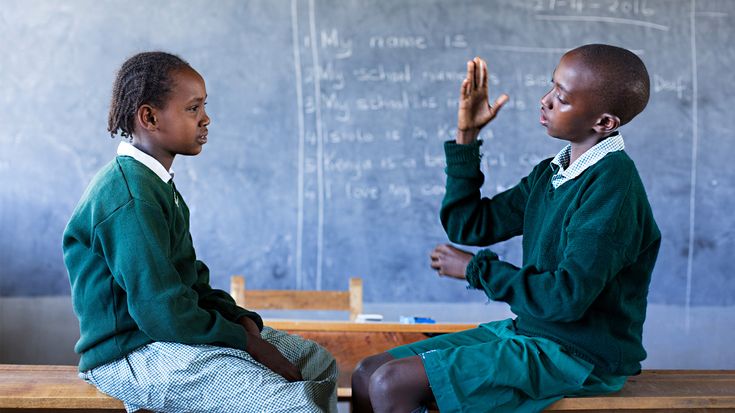 An image of 2 kids signing at each other in a classroom
