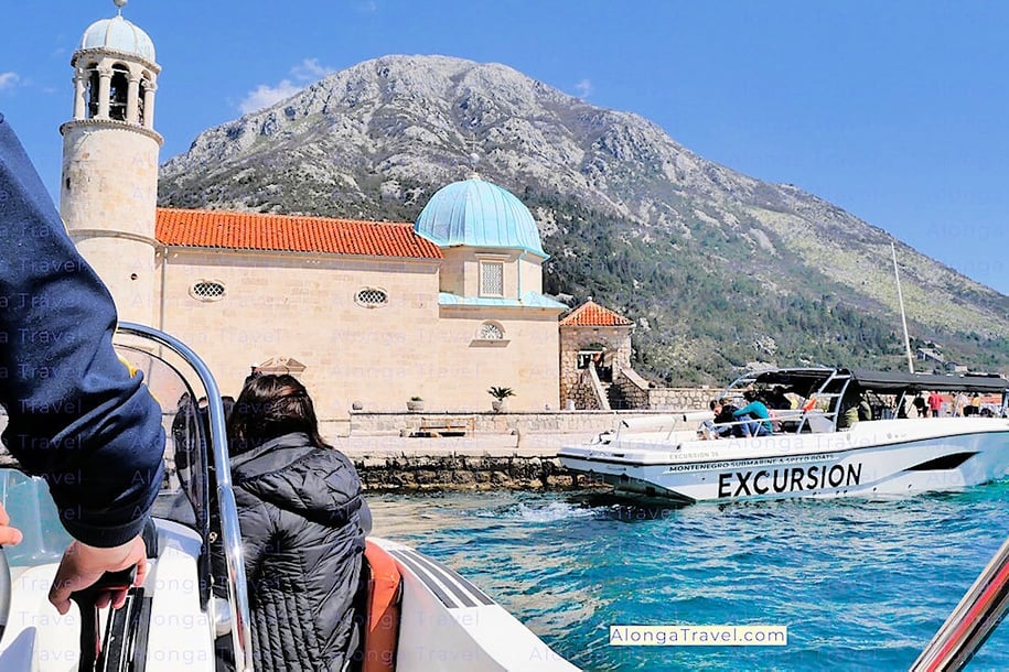 A blue cupola of The Lady of The Rocks sitting on an island is seen from my tour boat in Kotor