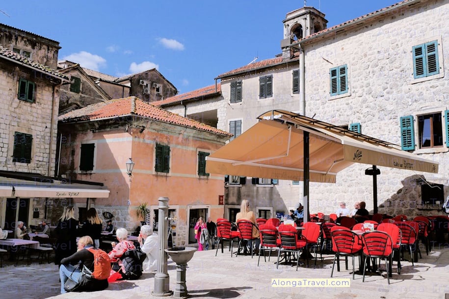 A cozy square in Old town Kotor with outdoor restaurant seating & people eating