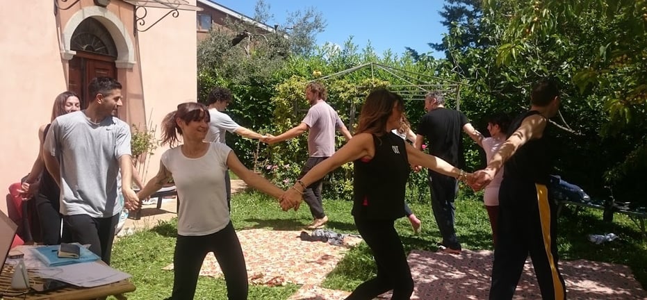 a group of people holding hands and dancing in a garden, classe di bioenergetica