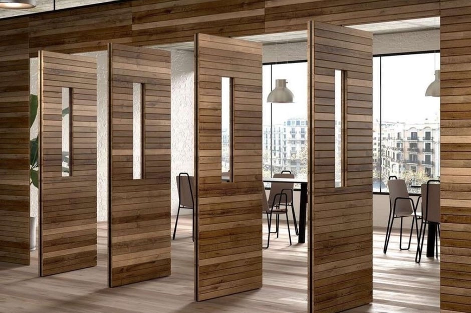 Puerta pivotante de gran formato en madera natural dentro de un espacio arquitectónico elegante