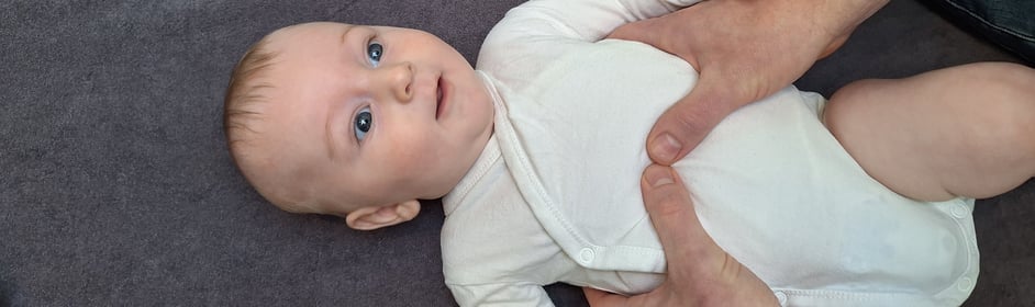een baby ligt op een tafel met 2 handen van een man