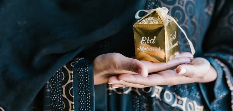 Donna che tiene in mano un pacchetto dorato con la scritta Eid Mubarak
