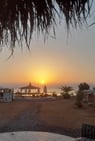 a sunset over a beach with a table and chairs