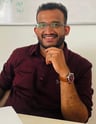 picture of R Arun in a maroon shirt and glasses sitting at a table