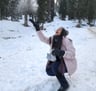 a woman in a pink coat and black boots is throwing snowballs
