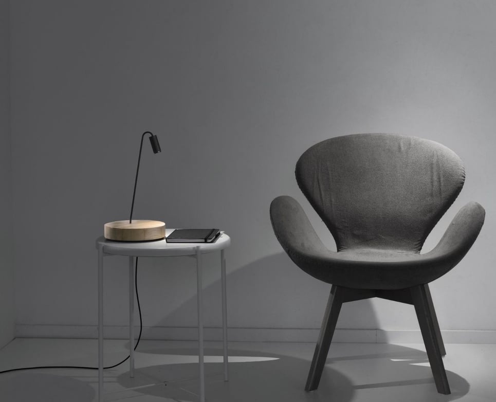 Lámpara de sobremesa con base circular junto a butaca en ambiente de lectura moderno