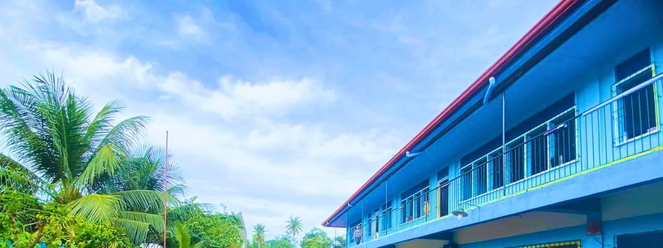 Blue grade school building with red roof and palm trees at Shelomith Learning Center, Inc.