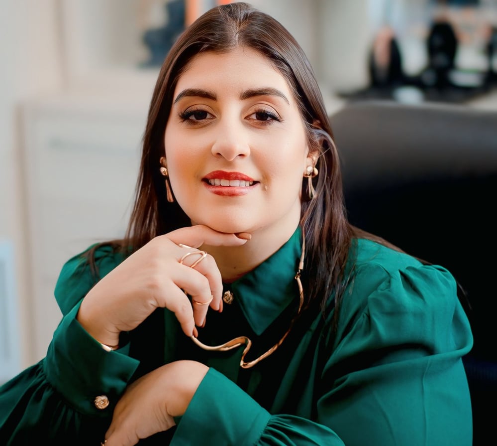 Foto da psicóloga sentada na cadeira do consultório, vestindo uma blusa verde escura e sorrindo