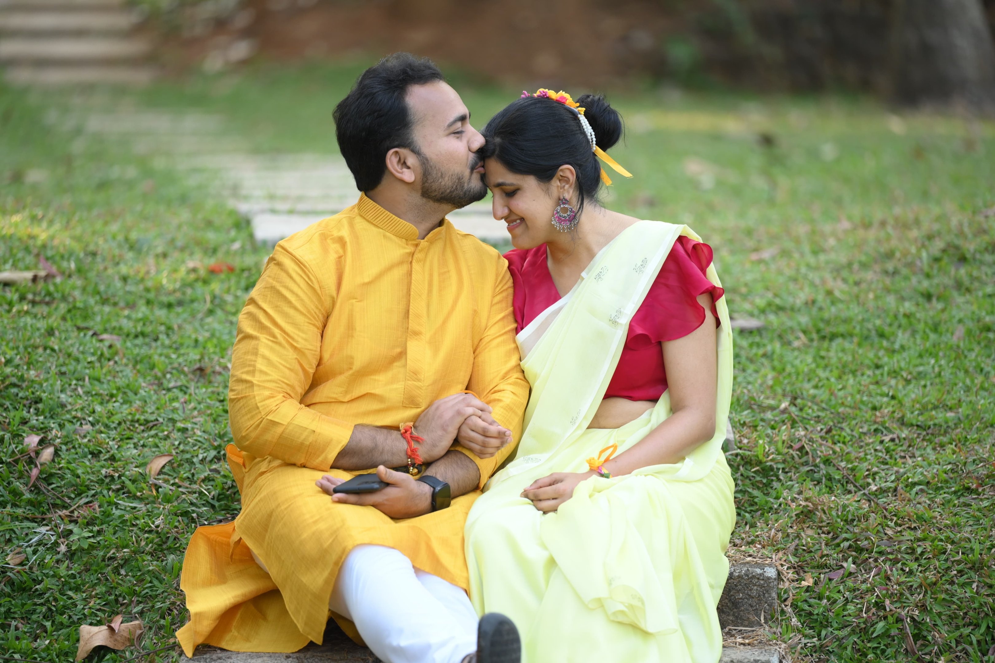 bride and groom in yellow dress sitting at the lawn and kissing during their haldi celebrations of the intimate wedding in Kerala