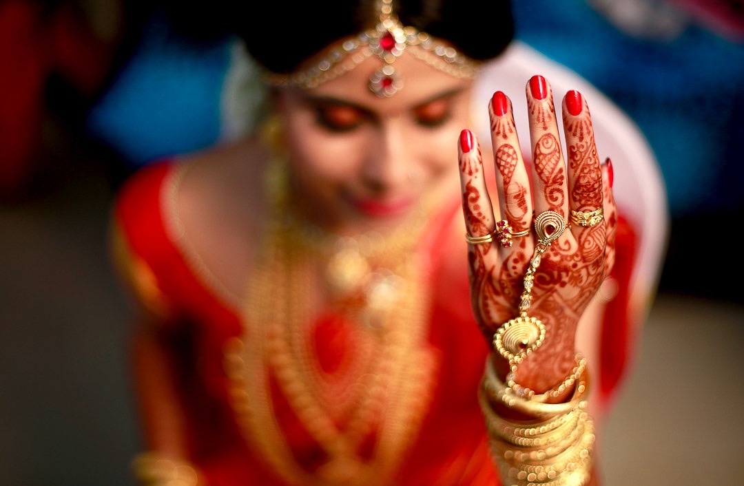 candid photograph of a kerala bride in red saree and ornaments during her bridal makeup session