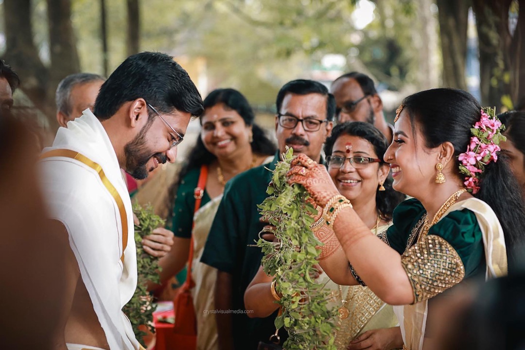 a traditional kerala wedding photography bride about to exchange kerala traditional garland made of tulsi leaves, she is laughing and all the relatives in the background