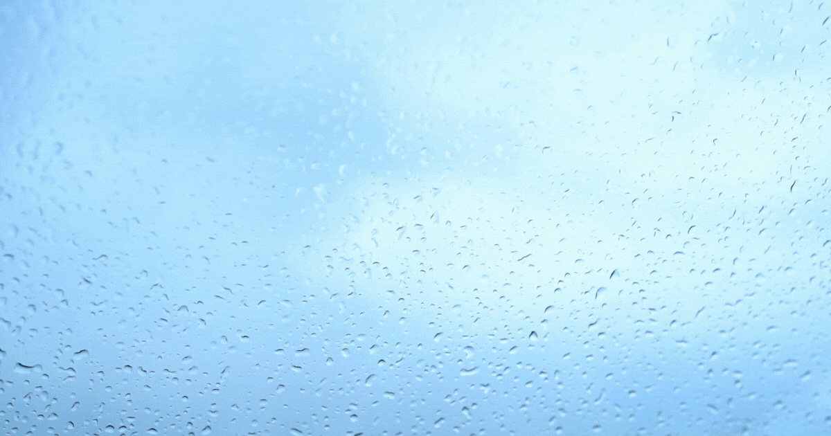 Close-up of a windshield wiper on a clear car windshield with water droplets in the background, illustrating visibility after