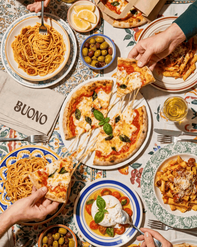 Flat lay of an Italian dinner table featuring Margherita pizza, spaghetti, penne pasta, and burrata cheese.