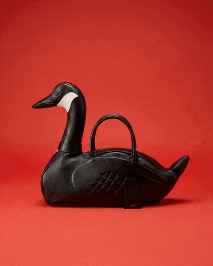 Unique black leather handbag shaped like a goose against a solid red background.