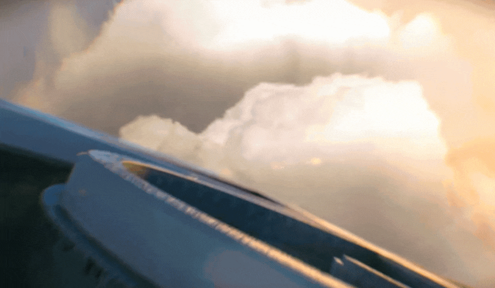Aerial view of soft white clouds from an airplane window during a golden sunset flight.